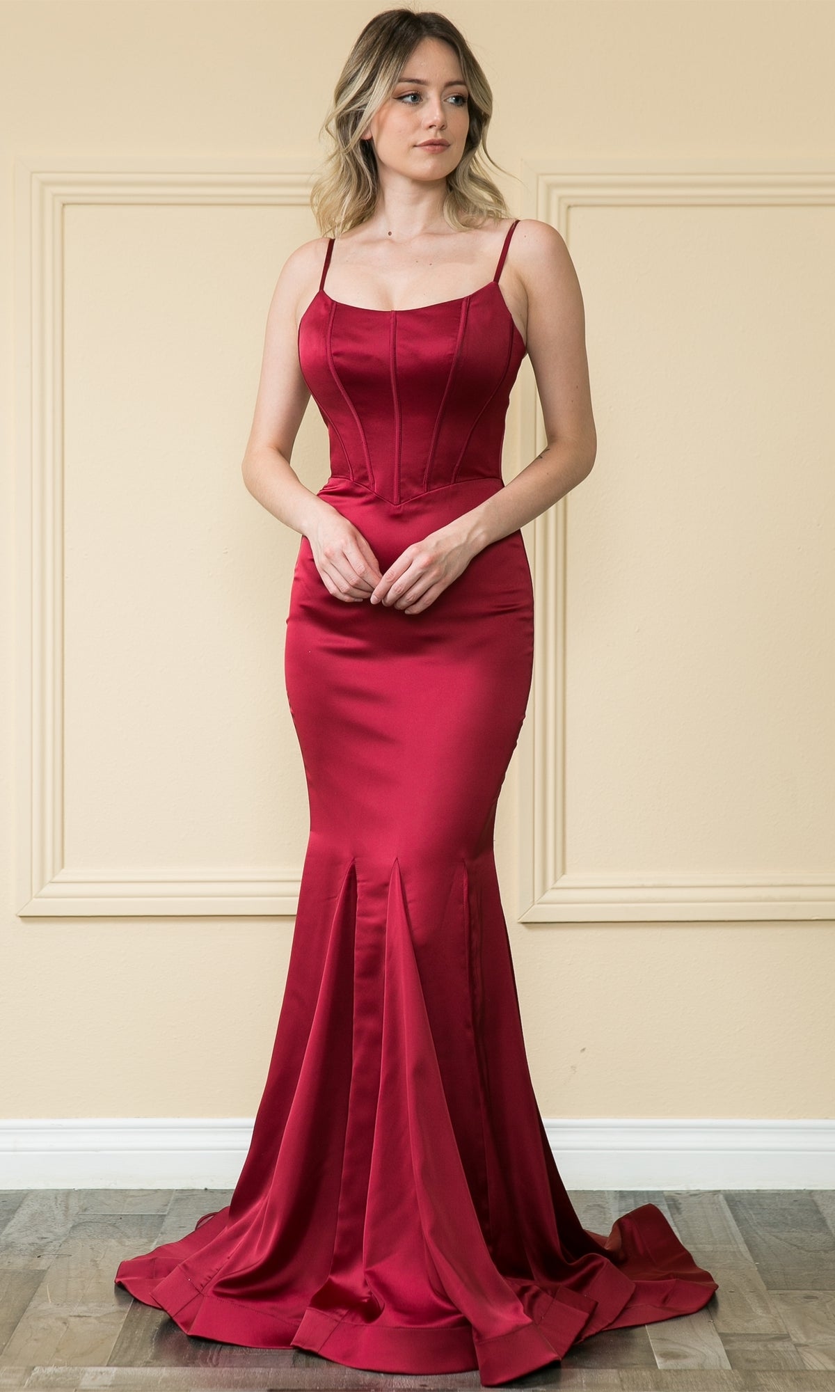 A woman stands indoors wearing the Stretch-Charmeuse Long Mermaid Prom Dress 9006, a fitted, floor-length, sleeveless red evening gown with thin straps and a mermaid silhouette.